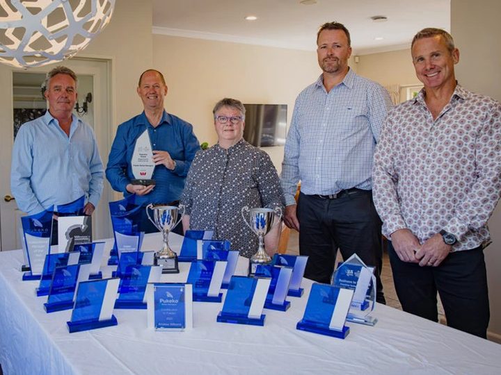 Pukeko rental managers behind a table of blue glass franchise awards and two silver trophies.